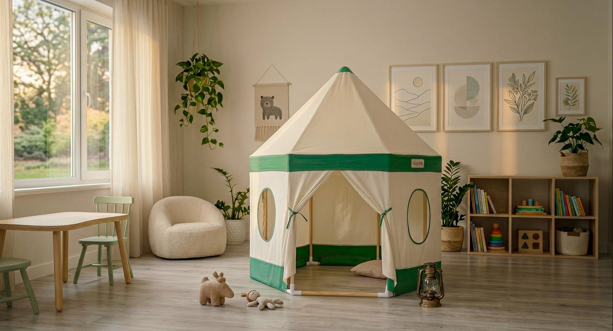 A children's play tent with a cream and green design stands in a beautifully styled child's room with a wooden table, chairs, bookshelves, and potted plants.